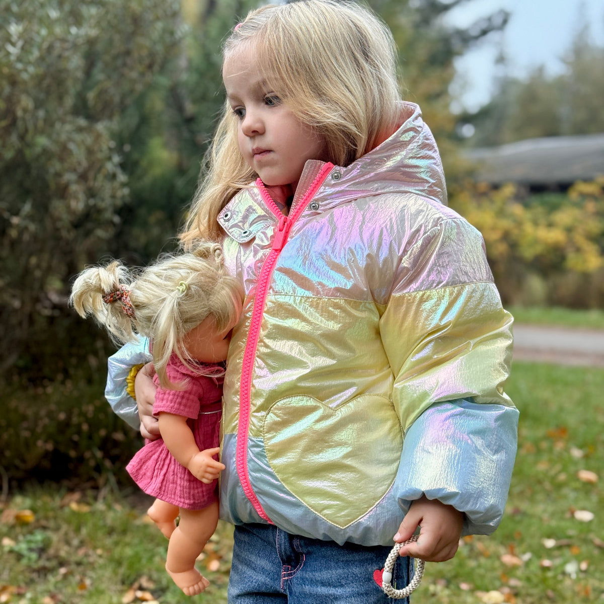 Child holding a doll outdoors with a colorful jacket