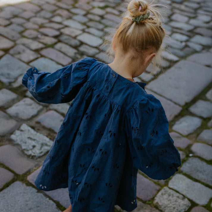 Child in a blue dress standing on a cobblestone street