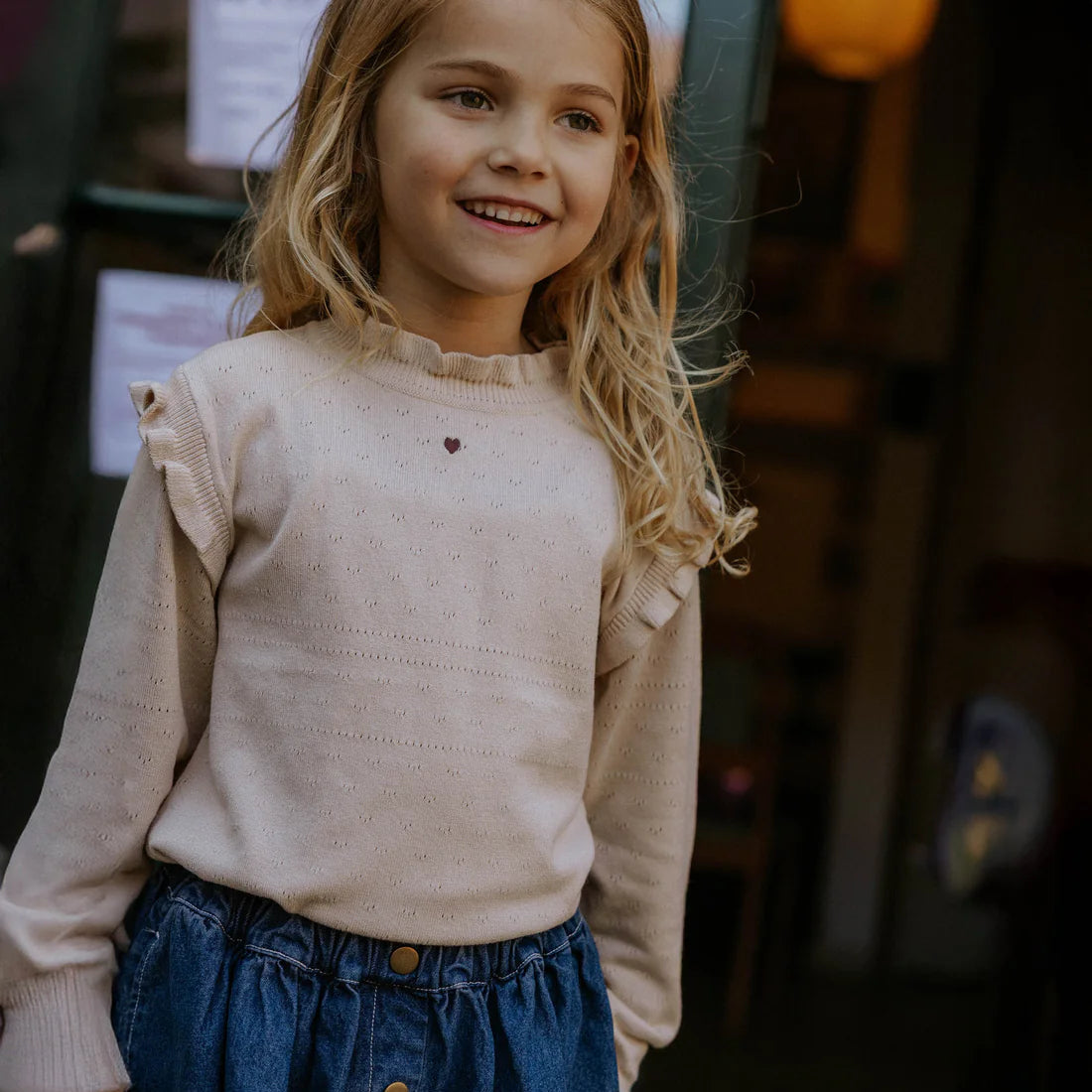 Young girl wearing a beige sweater and blue skirt with a blurred background