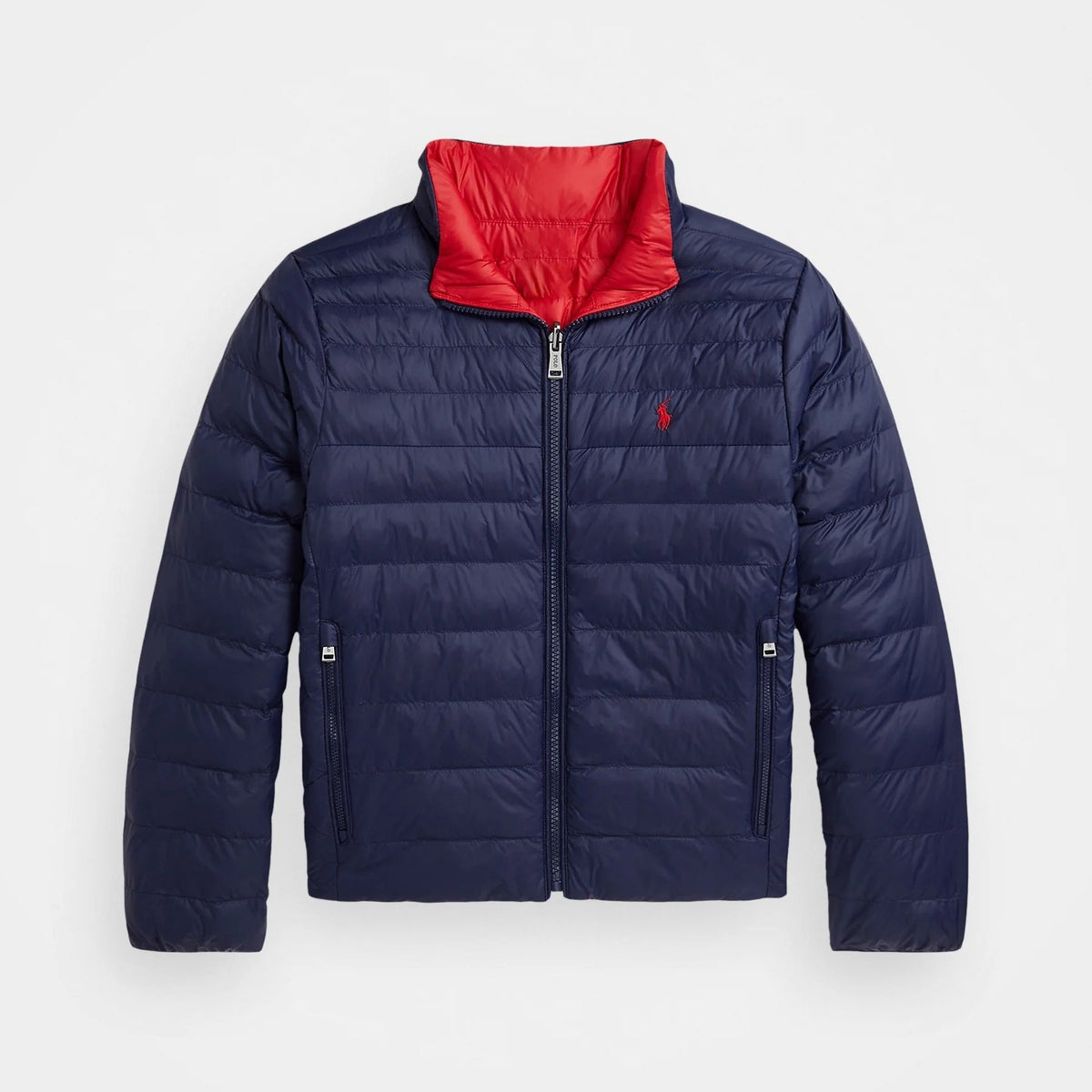 A navy blue puffer jacket with a bright red inner collar, featuring a front zipper, zippered side pockets, and a small embroidered polo player logo on the left chest, displayed against a light gray background.
