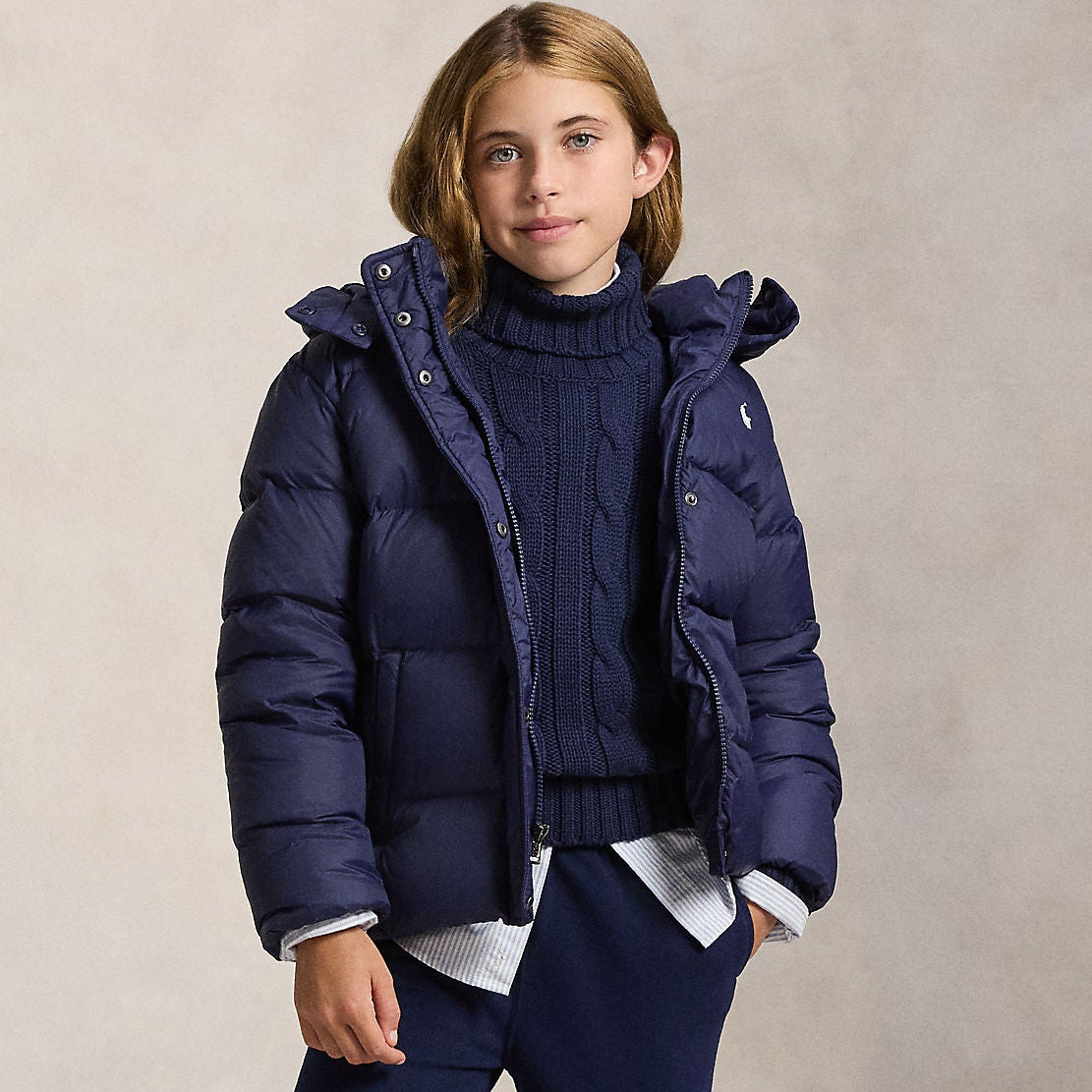 Person wearing a navy puffer jacket, sweater, and pants on a beige background