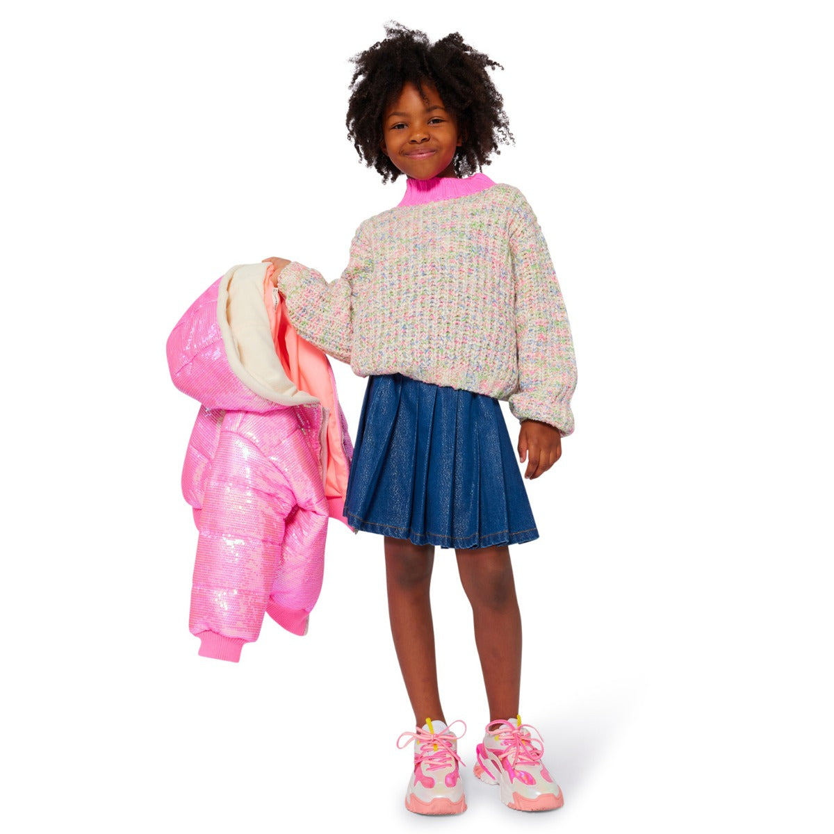 Child in denim skirt holding a pink jacket on a white background