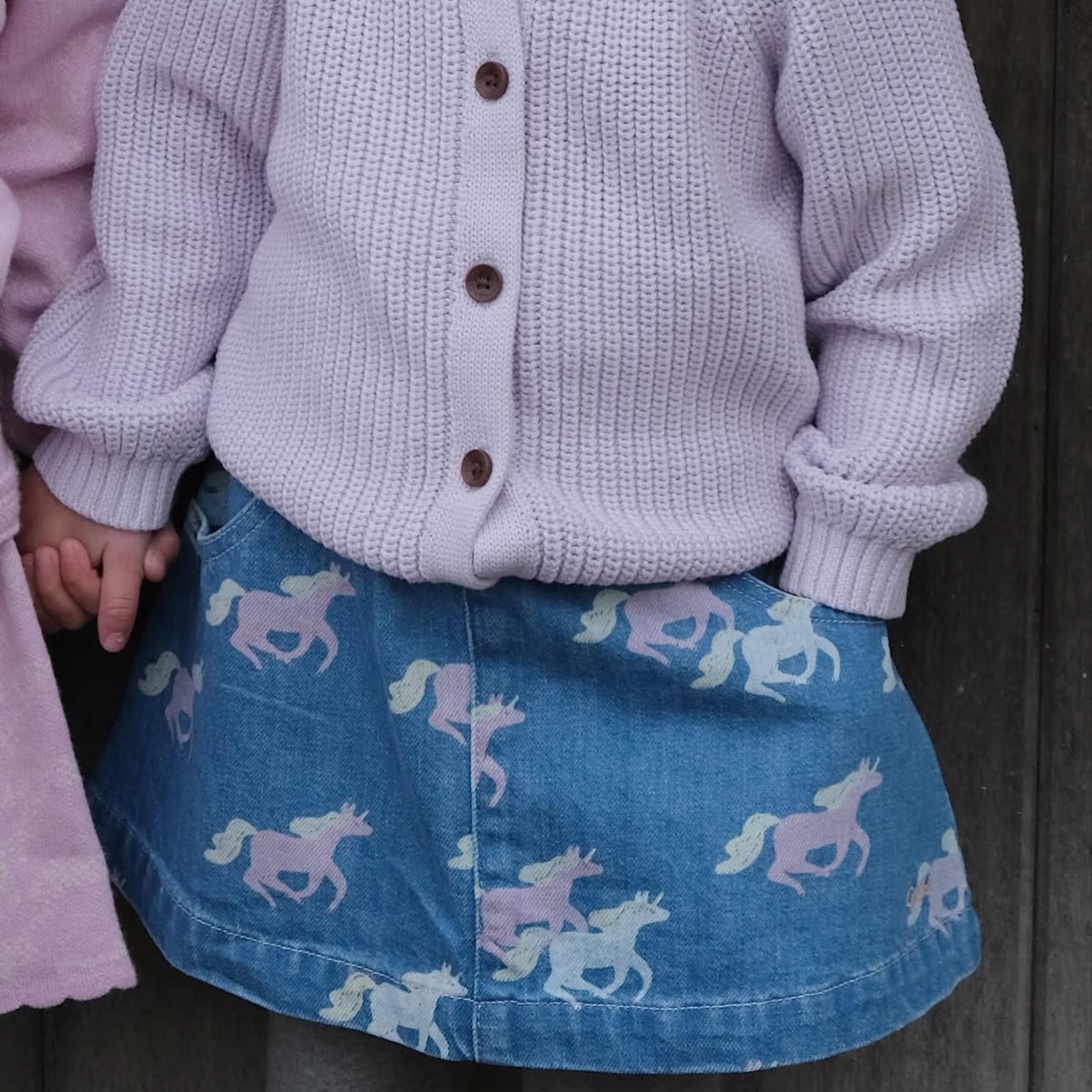 Child wearing a light purple cardigan and blue skirt with unicorn pattern.