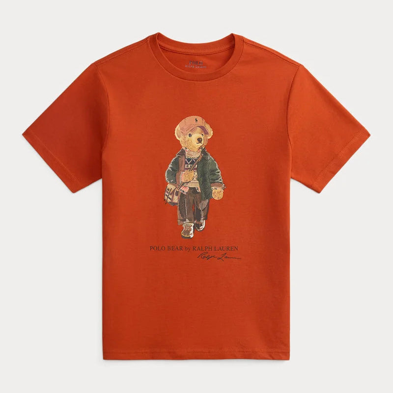 A short-sleeve crewneck t-shirt in a vibrant burnt orange color, featuring a central graphic of a teddy bear wearing a green jacket and brown pants, with 'PETER PADDY BEAR' text printed below.