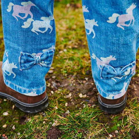 Blue jeans with unicorns and bow pattern worn outdoors on a grassy ground.