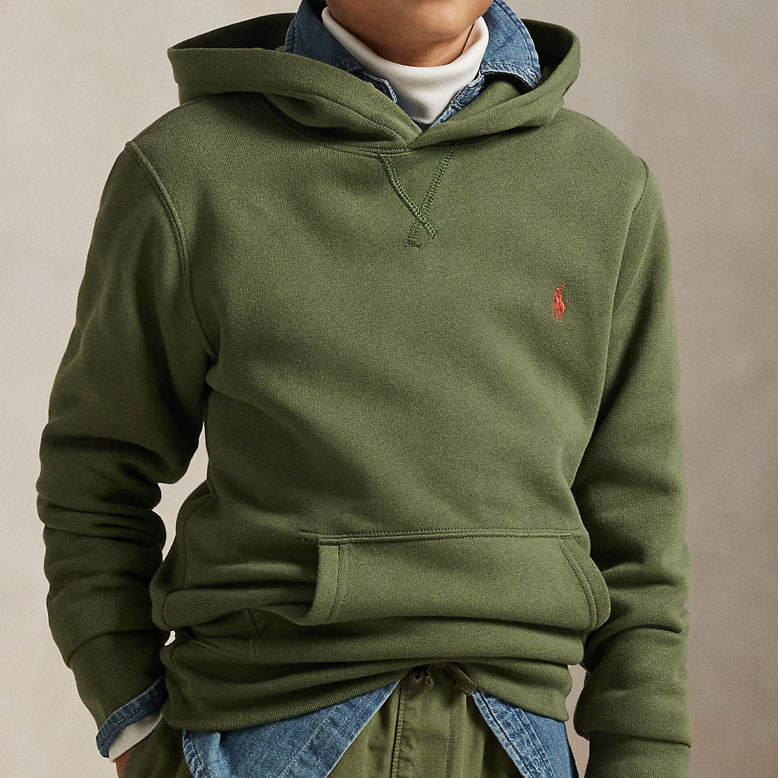 Young boy wearing a green hoodie with a small logo on a beige background