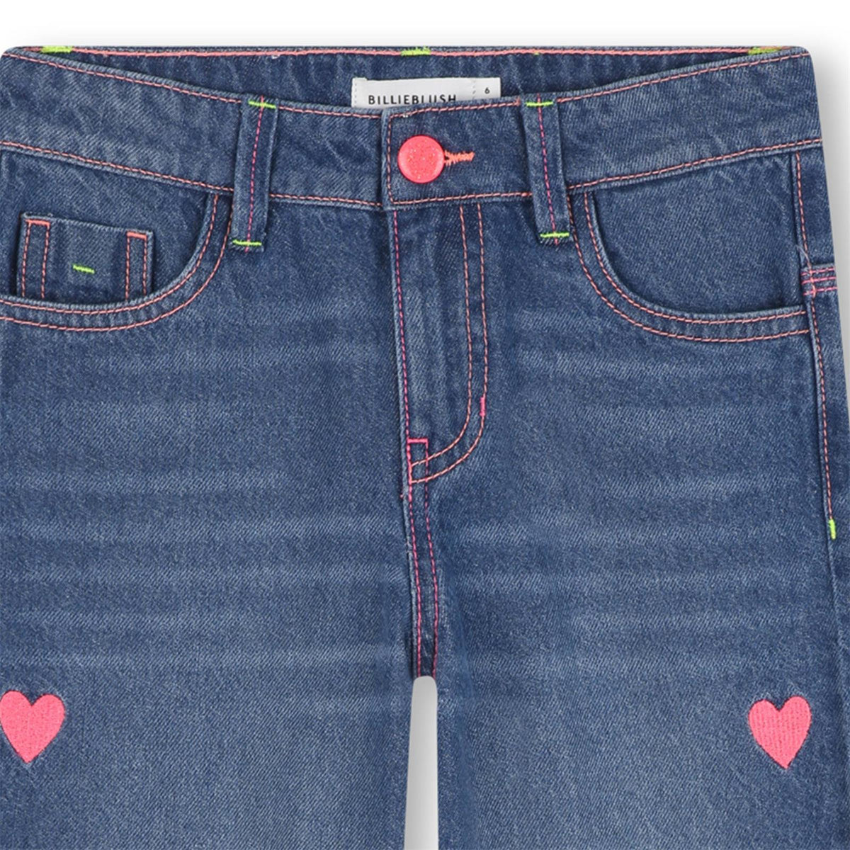 Close-up of blue jeans with pink heart designs and a visible brand label.