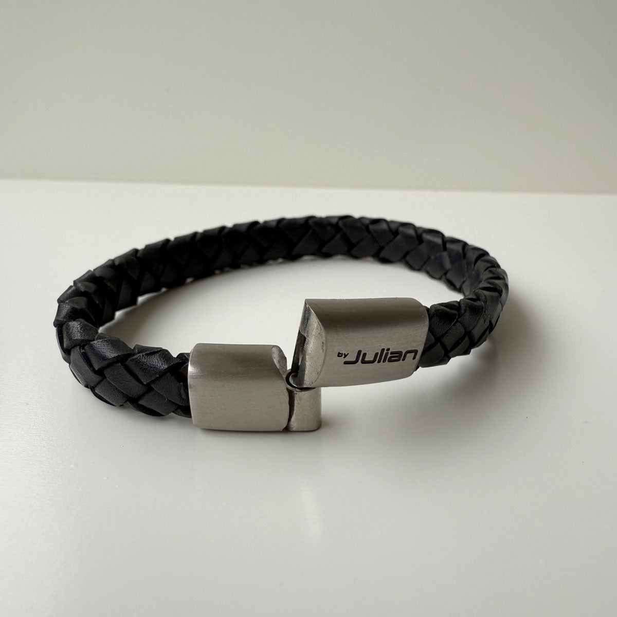 Black braided leather bracelet with open silver clasp on a white background