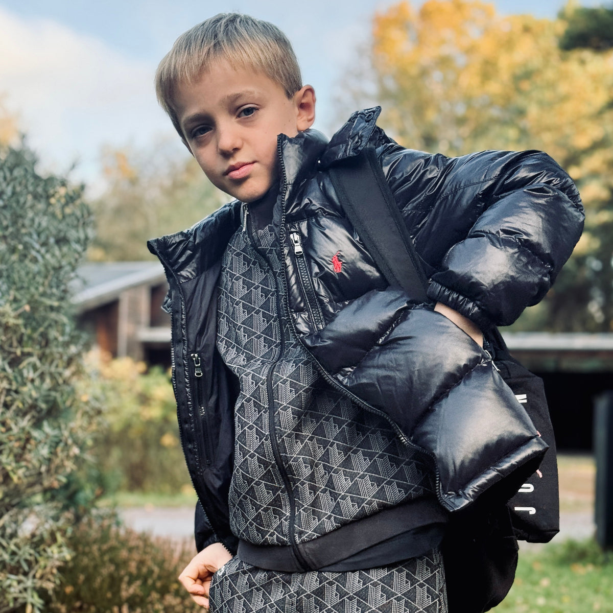 Kille i svart Ralph Lauren dunjacka med ryggsäck utomhus