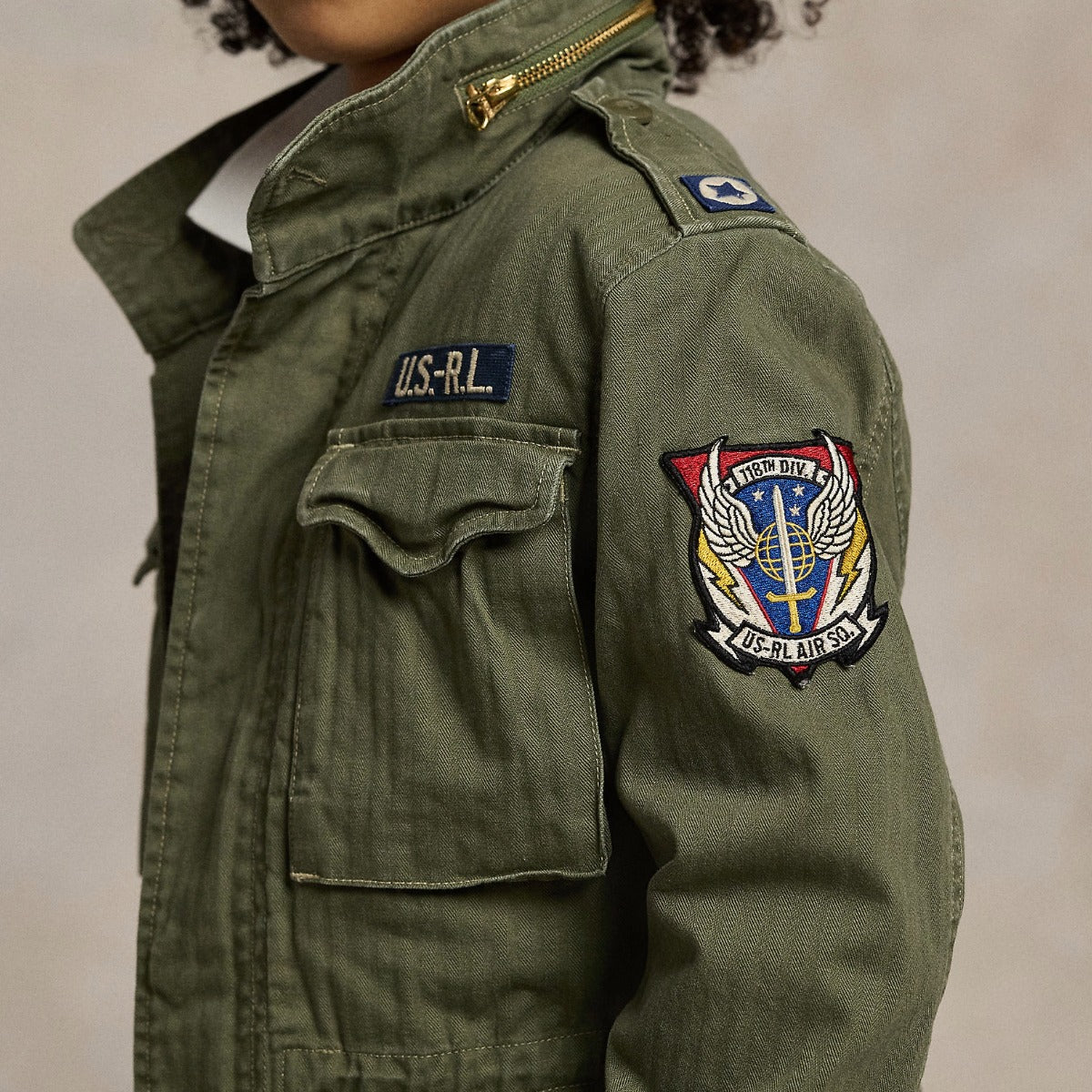 Green military-style jacket with patches on a neutral background