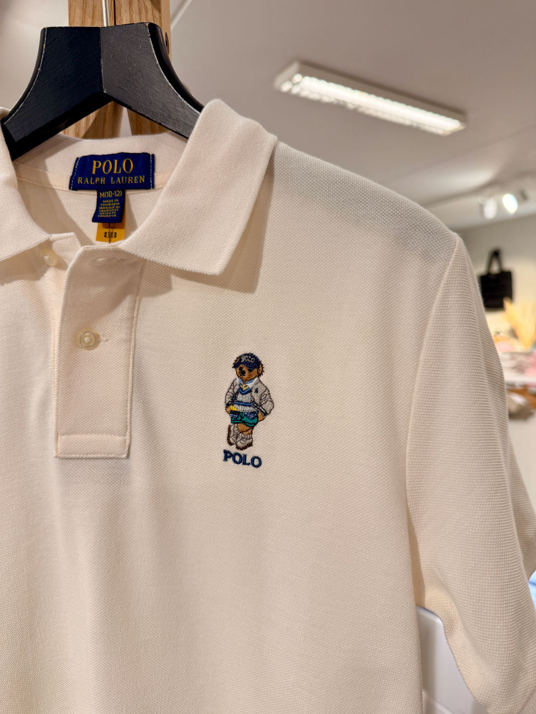 Beige polo shirt with embroidered bear logo on a hanger