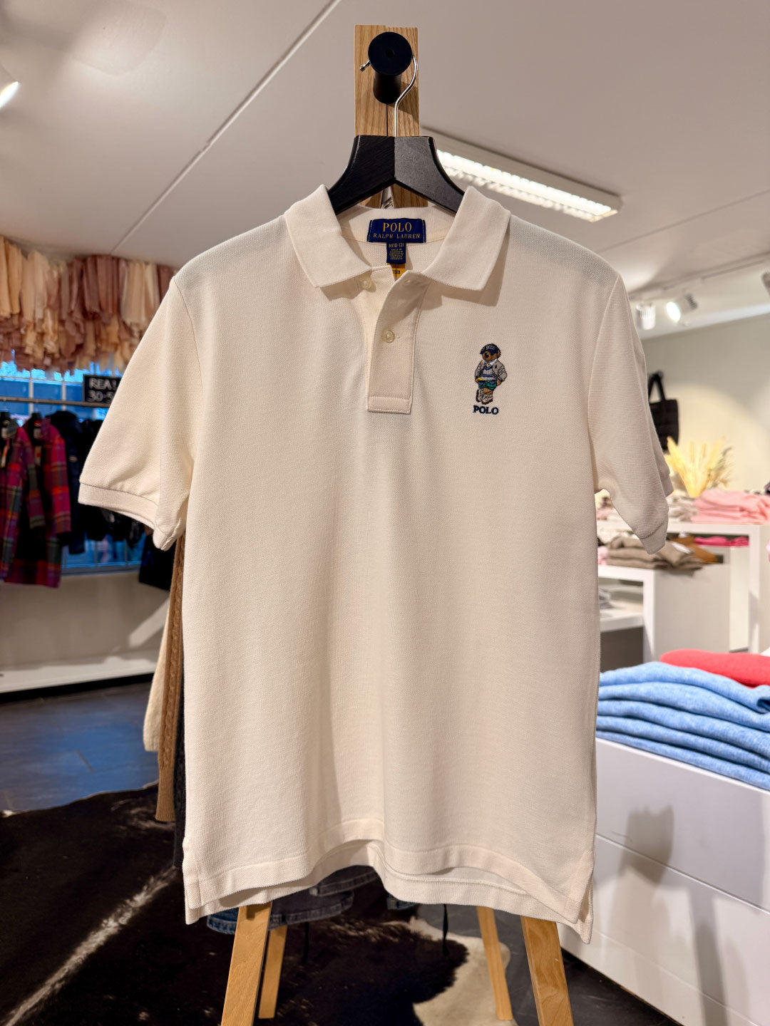 White polo shirt with a brand logo on a wooden hanger in a store setting.