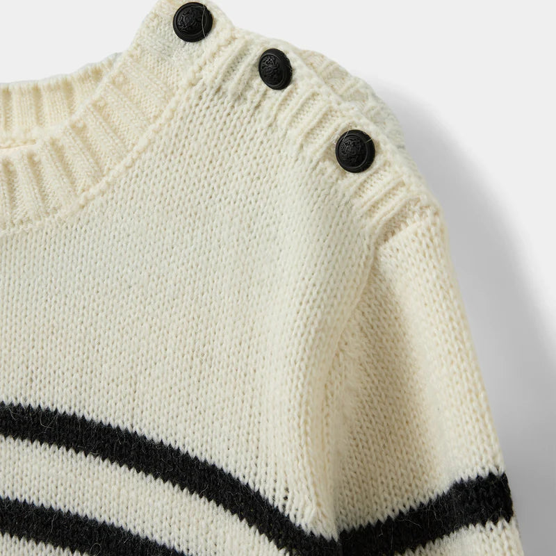 Close-up of a cream sweater with black stripes and buttons on a light gray background