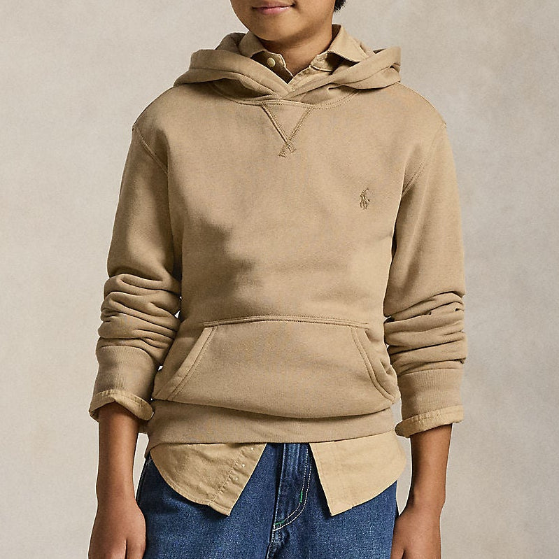 Teen boy wearing a beige Ralph Lauren hoodie and blue jeans against a neutral background
